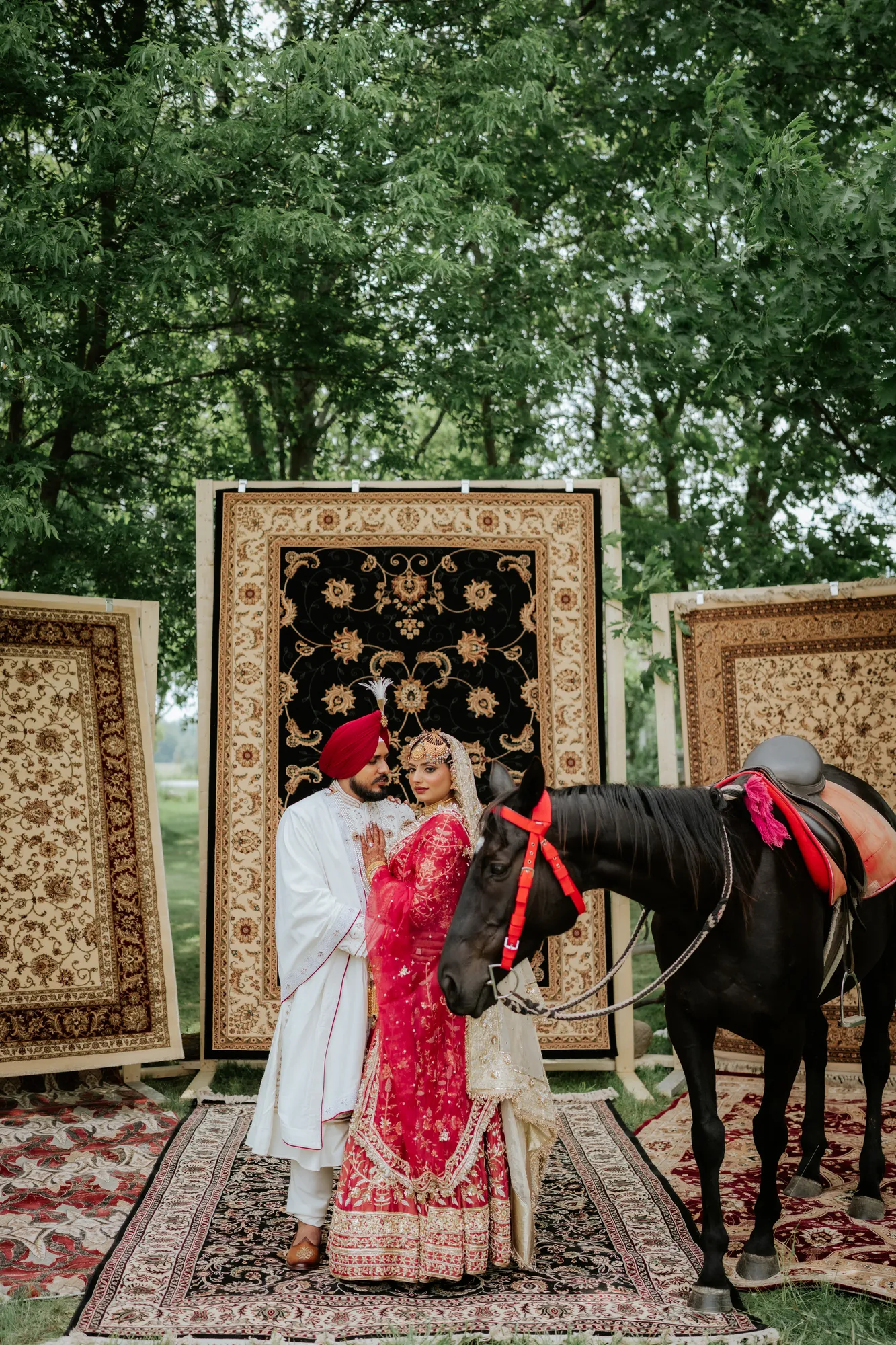 Bride and groom standing beside a black horse outdoors